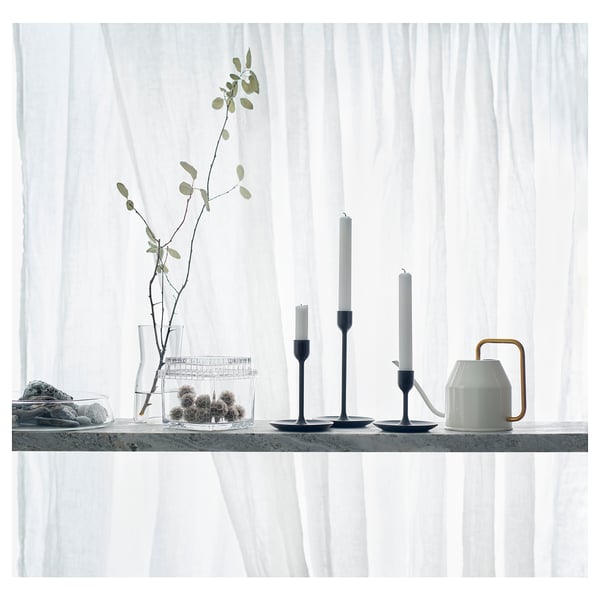 Aesthetic indoor setting with a black watering can on a sleek marble shelf, accompanied by candles and minimalist decor.