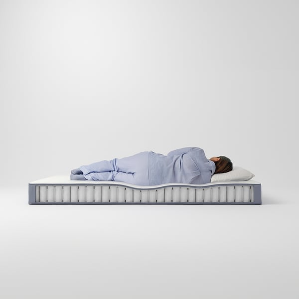 A person sleeps on a light blue VESTERÖY mattress with grey sides, featuring pocket springs and foam topper, guaranteed for 10 years.