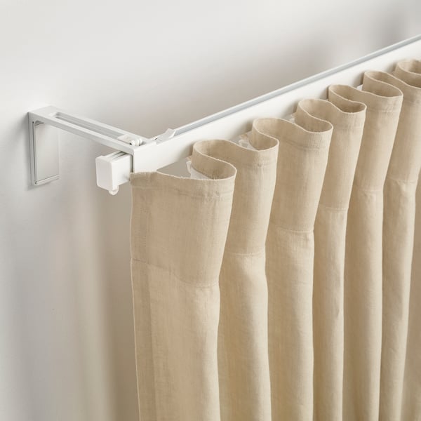 Curtain rod holds light or heavy curtains. Wall-mounted, lets light in or blocks it. Via white rail and hooks.