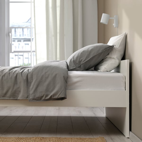 A minimalist bed frame with grey bedding and a wall-mounted light. Clean lines, versatile design, and storage options underneath.