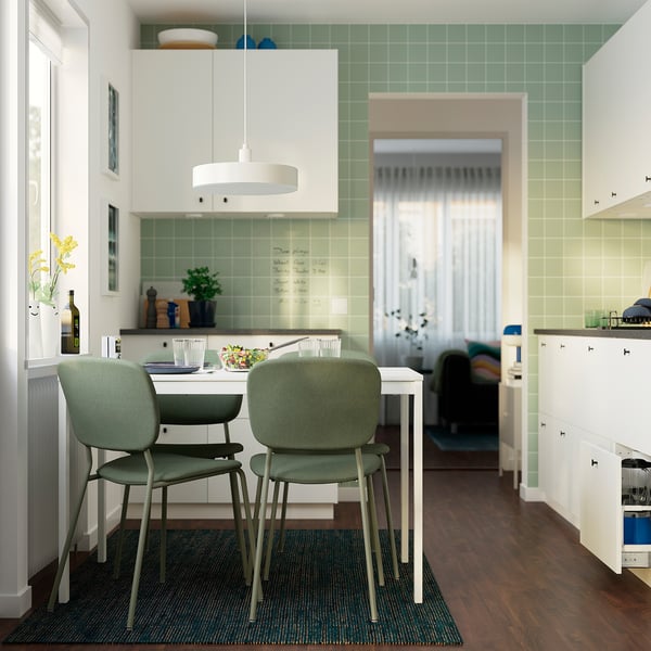 Small kitchen with white extendable table, green chairs, and green-tiled backsplash. Brightened by natural light, its cosy for dining.