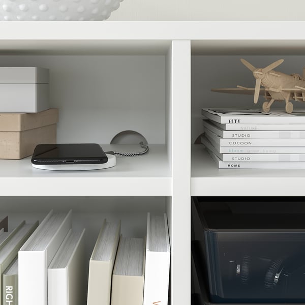 White bookshelf with black gadget, books, and wooden plane model.