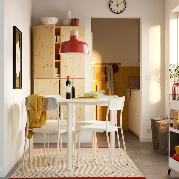 Modern kitchen with white table, red light, wooden shelves, bowls, wine, yellow throw, rug, doorway.