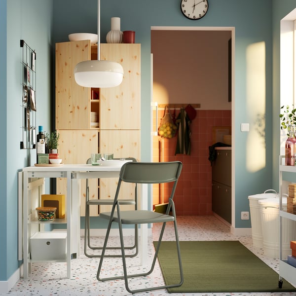 Modern kitchen with small white table, green chairs, wood cabinets, and hanging lights.