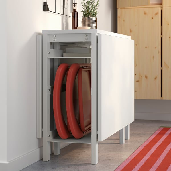 White VIHALS foldable dining table with red chairs stored inside, set against a light wooden cabinet.