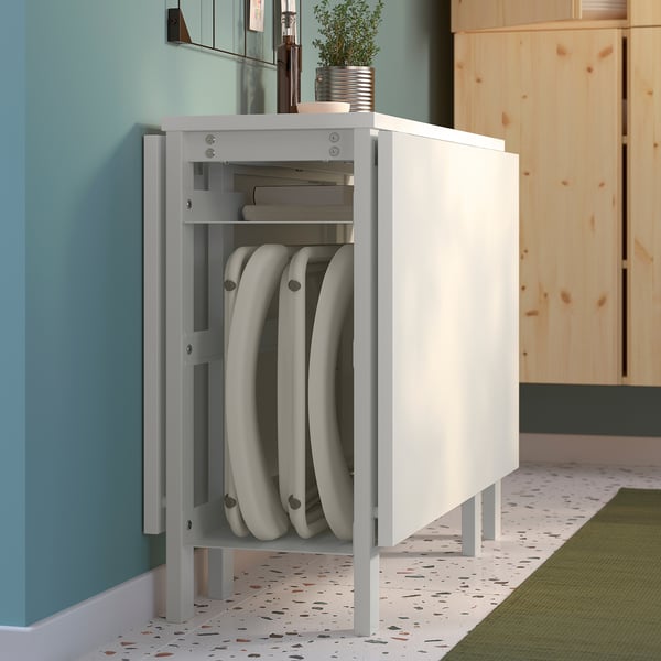 A white storage cabinet holds stacked white folding chairs and a few books, with a potted plant on top. Ideal for compact living.