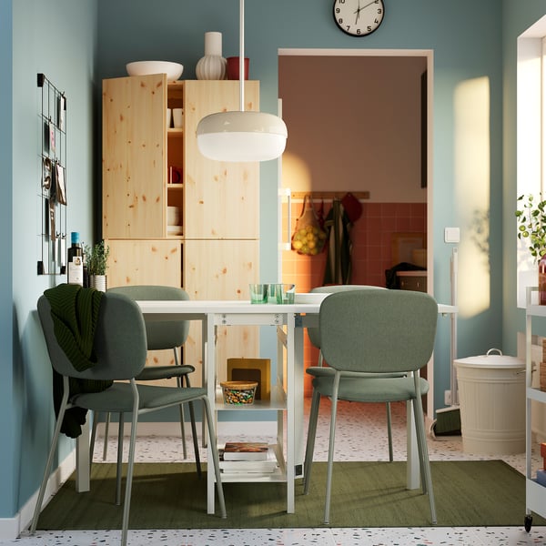 Modern dining space with white VIHALS table and green chairs. Light wood cabinets, blue walls, and a room divider visible in the background.