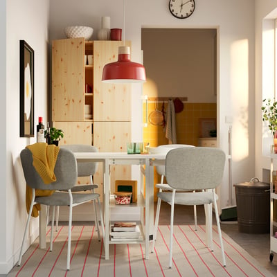 Small dining set with white metal table and grey chairs, wooden cabinet, red lamp.