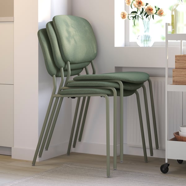 Three green upholstered chairs stacked neatly, ideal for space-saving in a bright, minimalist room.