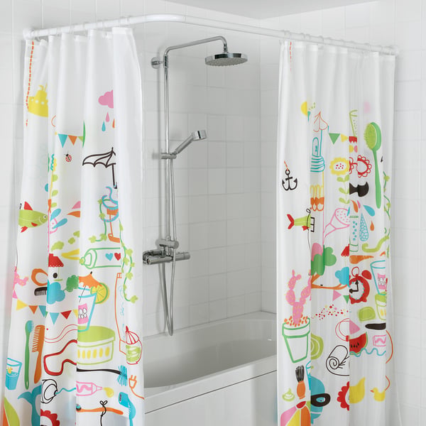 Brightly patterned shower curtain with various objects hangs in bathroom; white tiles and chrome shower head visible.