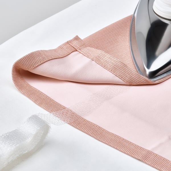 Ironing pink room-darkening curtains with heading tape for easy hanging.