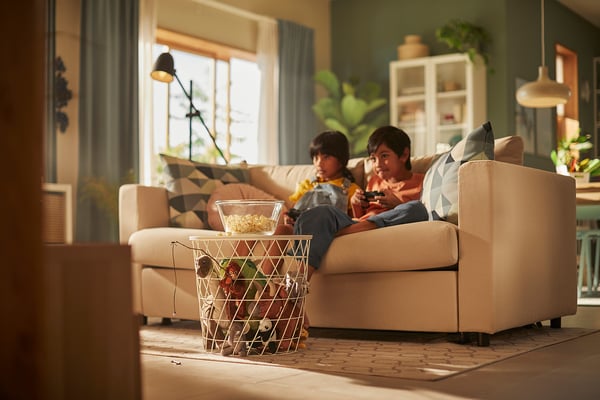 Kids gaming on VIMLE sofa with snacks & plants in sunny room.