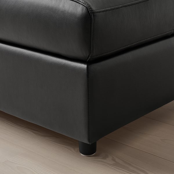 Close-up of black leather couch, showcasing smooth, stitched fabric & sturdy wooden leg.
