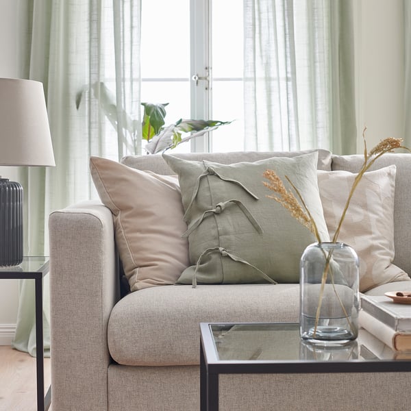 Modern beige sofa with plush cushions and green pillow on glass table.