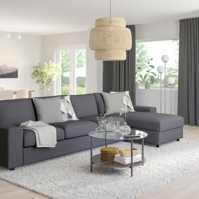 Modern living room with grey sofa, pillows, pendant lamp, coffee table, window, and rug.