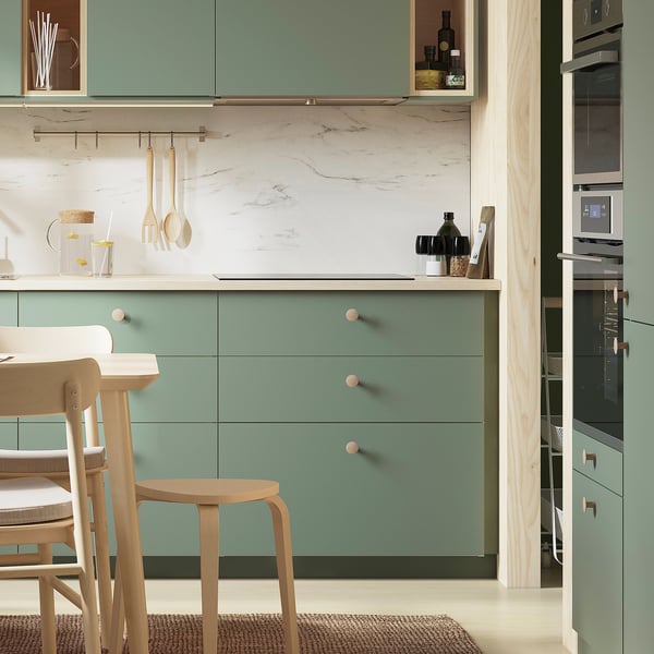 Modern kitchen with light green cabinets and wooden stools. Knobs are small, round, and made of light wood.