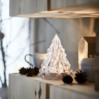 Clear geometric christmas tree lamp on wooden shelf; smaller than pine cones and kettle.
