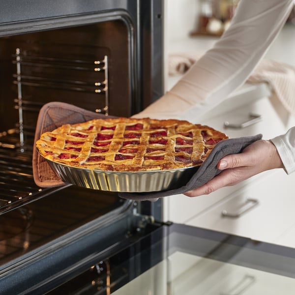 A person holding a baked pie with a lattice top in a pie dish, ready to be placed in the oven.