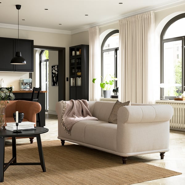 Contemporary living room with beige sofa, wooden table, peach chair, black light, bookshelf, and arched windows.