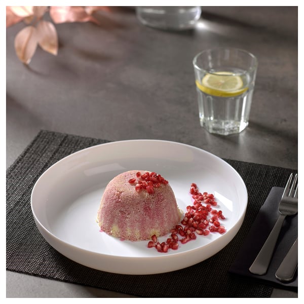 Opal glass dessert plate with cake and pomegranate seeds. Silverware on dark placemat. Lemon water glass.