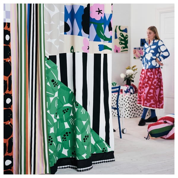 Vibrant room with colourful abstract curtains & patterns. Person in blue & white polka dot outfit stands near.