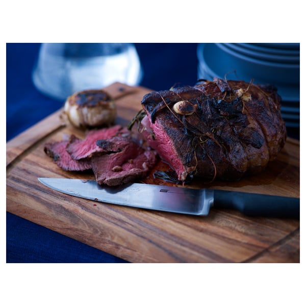 A knife on a cutting board with grilled meat.