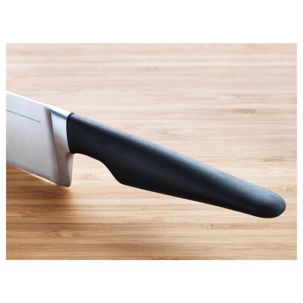 Large kitchen knife with dark handle rests on wooden surface. Stainless steel blade suggests durability and sharpness.