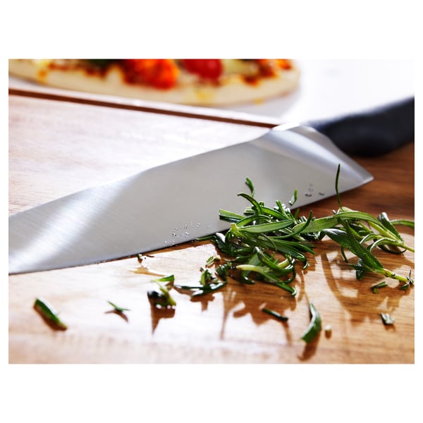 A sharp, quality knife rests on a wooden board, chopped herbs scattered nearby, indicating precise and efficient cutting.