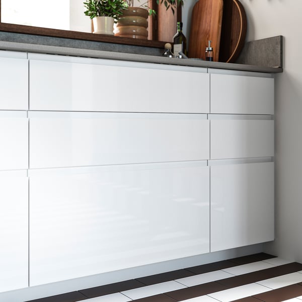 Modern kitchen cabinets with white glossy finish, sleek handles, and dark flooring.