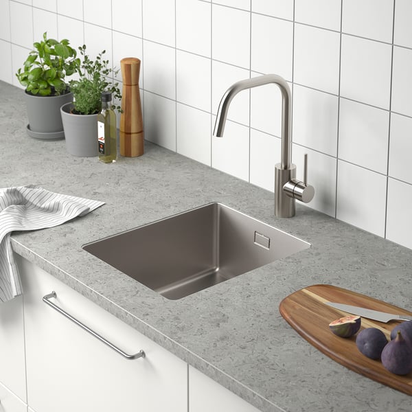 Modern kitchen sink with stainless steel faucet, cutting board, fruit, and herbs.