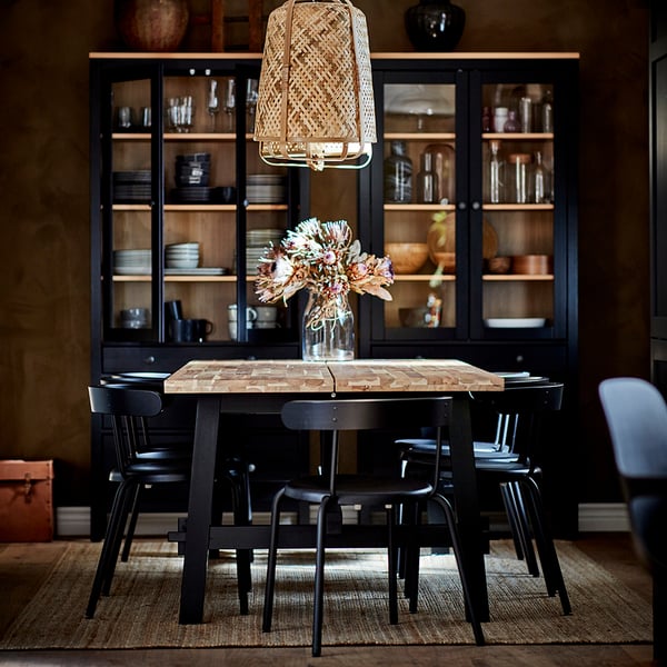 Cosy dining setup with YNGVAR black chairs around rustic table, under black cabinet with glass doors.