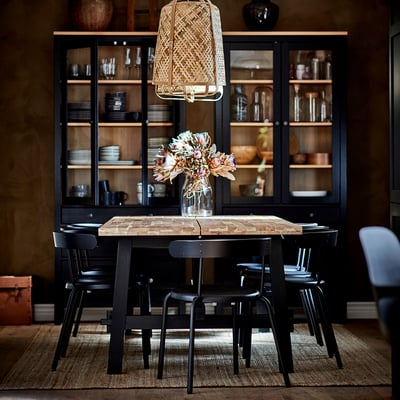 Cosy dining setup with YNGVAR black chairs around rustic table, under black cabinet with glass doors.