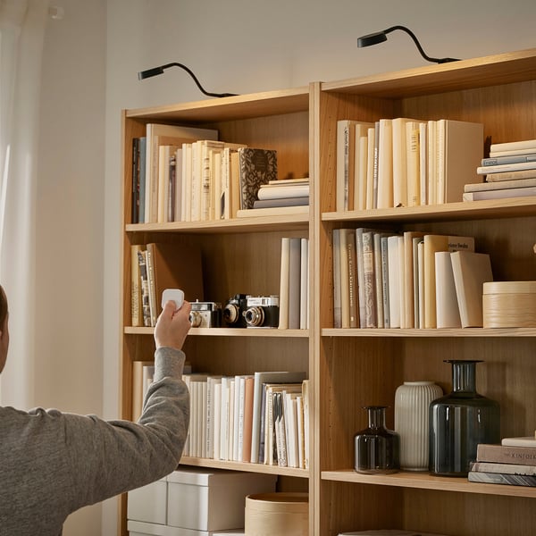 Adjusting lamp over wooden bookshelf with books and vases.