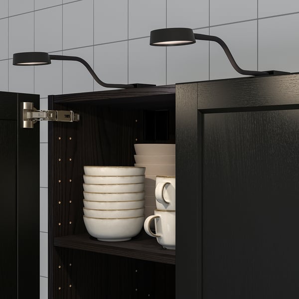 Black cabinet with bendable led lights, illuminating stacked white bowls and mugs, showcasing flexible lighting.