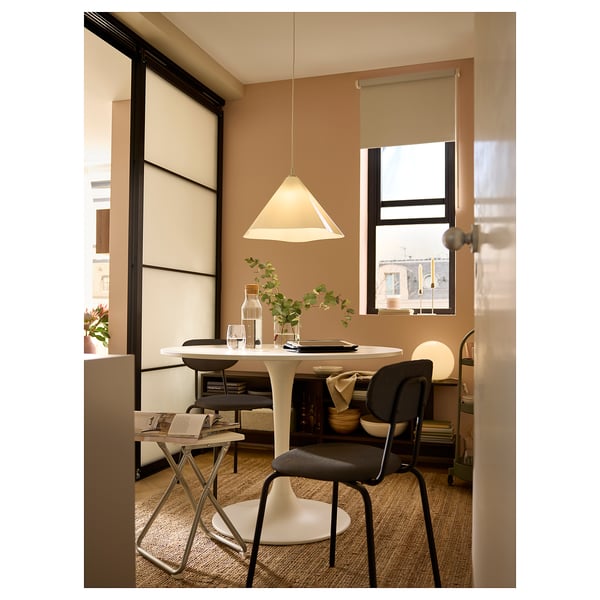 Modern dining area with round table, ZEBRASÄV lamp, vases, glasses, plants, and bright window.