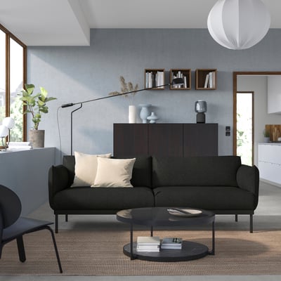 Moderni svetainė su pilka sofa ÄPPLARYD, juodu kavos staliuku, mediniu stalviršiu ir pakabinamu šviestuvu.