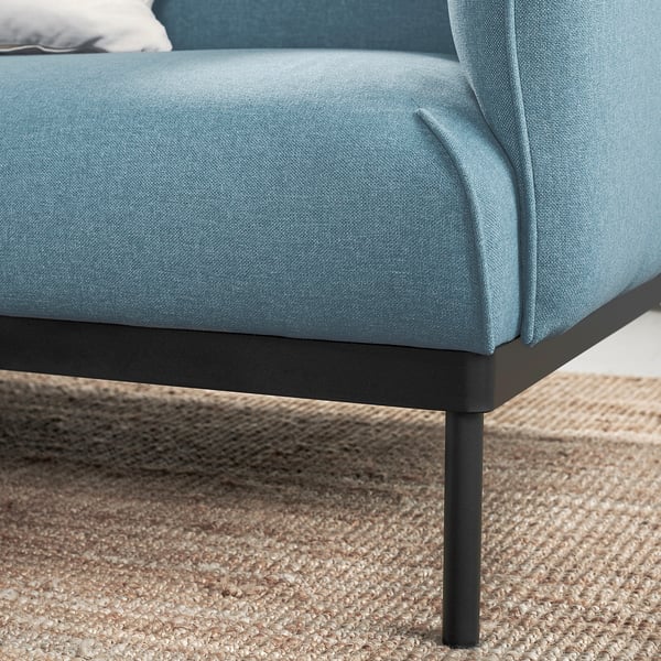 Mėlyna minkšta sofa su metalinėmis kojomis ant džiuto kilimėlio.