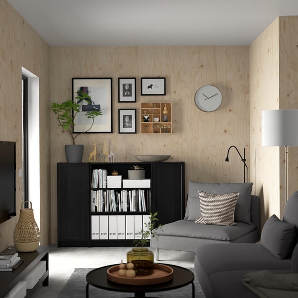 Minimalistinė svetainė su BILLY knygų spinta, pilka sofa, medinėmis sienomis ir dekoracijomis.