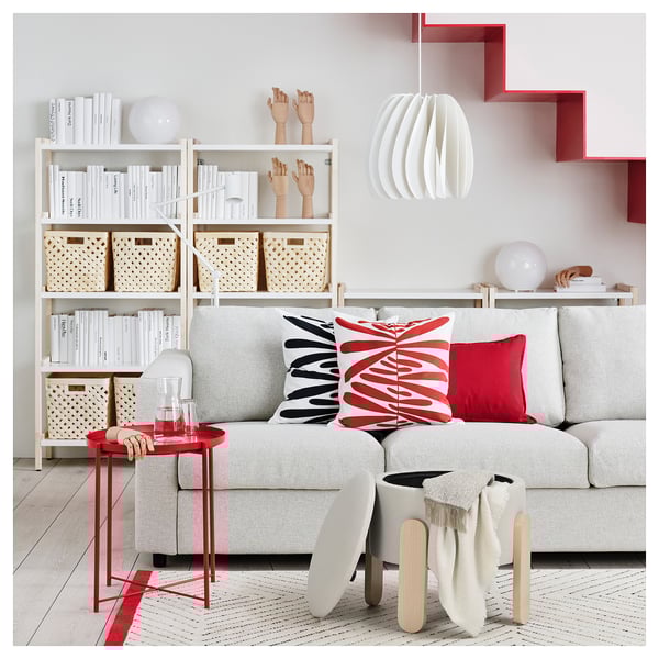 Moderni svetainė su šviesiai pilka sofa, spalvingomis pagalvėmis, mediniu šoniniu stalu ir balta knygų lentyna su įvairiais daiktais.