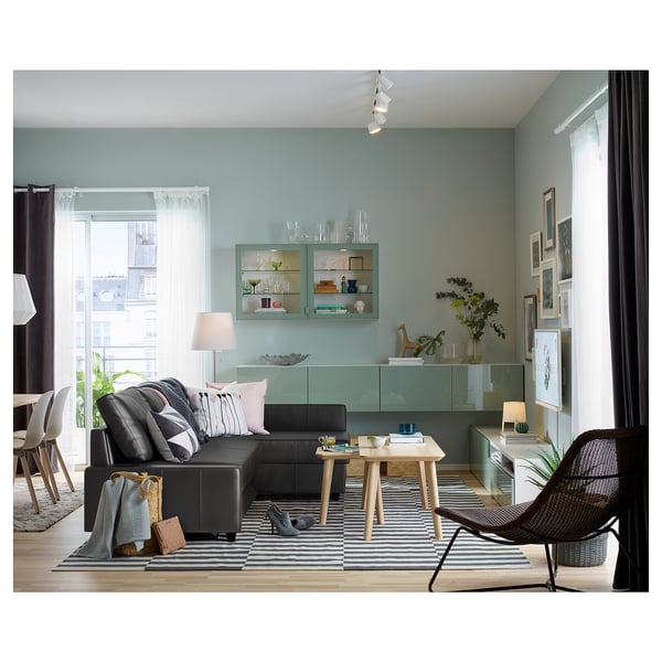 Moderni svetainė su juoda odine L formos sofa, dryžuotu kilimu, stiklinėmis spintelėmis ir dideliais langais.