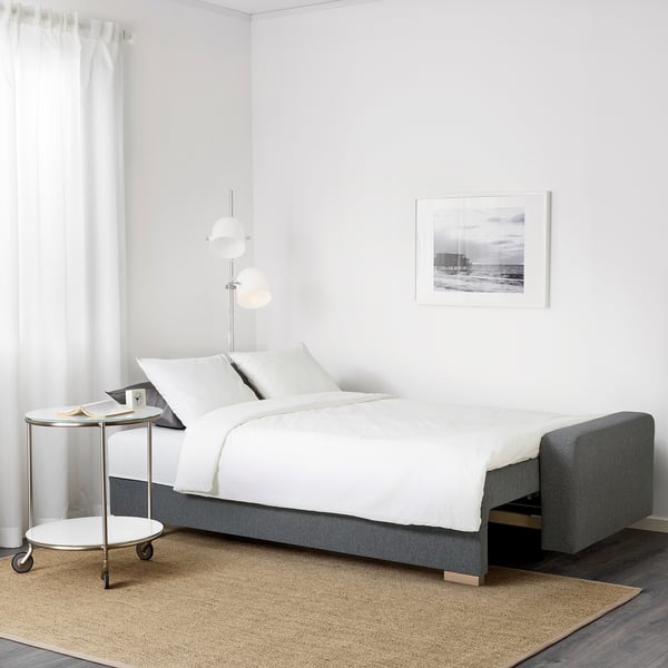 Modernus miegamasis su sofa-lova GRÄLVIKEN, balta patalyne, šoniniu stalu ir paplūdimio tematika.