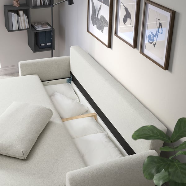 GRUNNARP sofa-lova su pagalvėlėmis, su sėdimomis ir miegamosiomis vietomis. Meno kūriniai ir lentynos fone.
