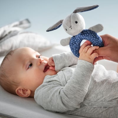 Kūdikis žaidžia su minkštu žaisliniu barškučiu, stimuliuojančiu klausą ir regėjimą, tinkamu nuo gimimo.