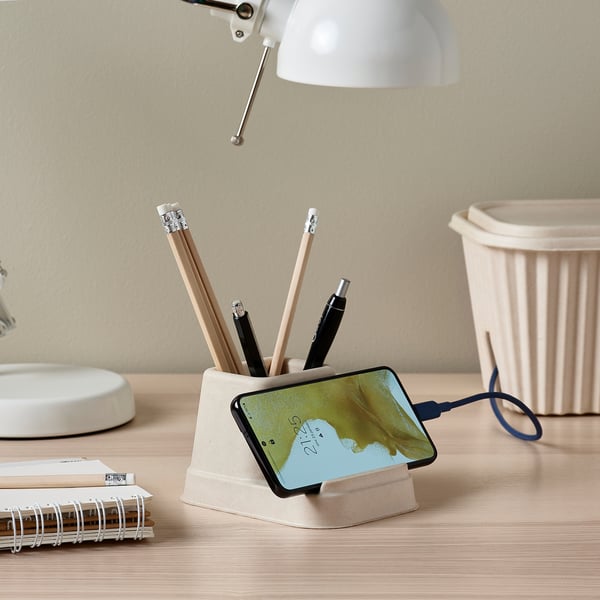 Smėlio spalvos organizatorius ant stalo laiko išmanųjį telefoną, rašiklius ir įkrovimo laidą. Netoliese esanti lempa ir užrašų knygelė.