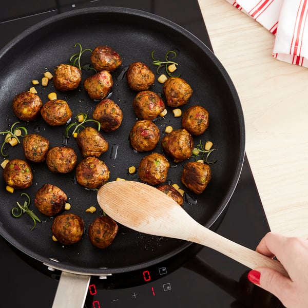Keptuvėje kepkite bulvytes veganiškais mėsos kukuliais, juos paruduodami. Mediniai mentelių mišiniai; raudoni nagai. Juoda keptuvė, viryklė, valdoma liečiant.