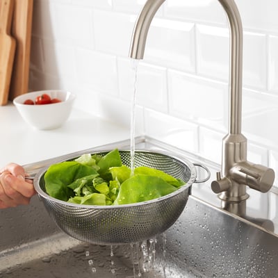 Asmuo skalauja salotas nerūdijančio plieno kiaurasamtyje po virtuvės čiaupu.