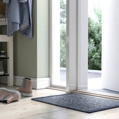 Mėlynas austas kilimėlis prie rožinių batų, po kabančiu pilku paltu.