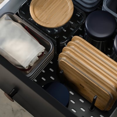 Sutvarkytas virtuvės stalčius su IKEA 365+ bambukiniais indais. Apvalios ir stačiakampės formos, tvarkingai laikomos. Baltas audinys ir tamsūs dangteliai aplink juos.