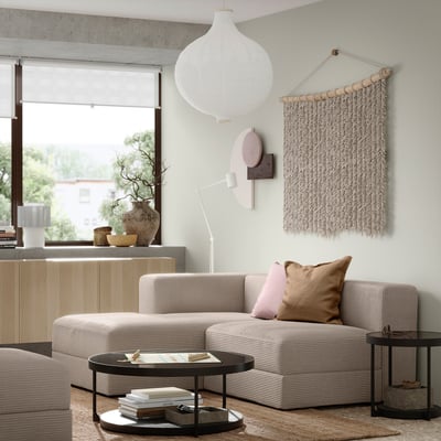 Moderni svetainė su smėlio spalvos JÄTTEBO moduline sofa, mediniu šoniniu staliuku, apskritu kavos staliuku, pakabinamu šviestuvu ir sienų menu.