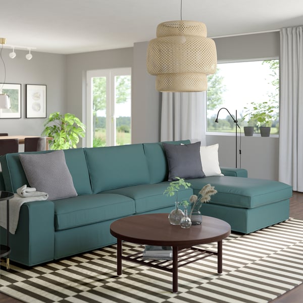 Moderni svetainė su KIVIK teal sofa, dryžuotu kilimu, mediniu kavos staliuku ir balta pakabinama lempa.